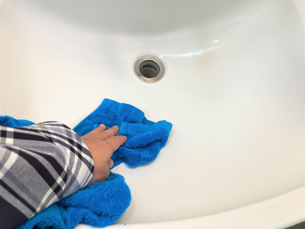 洗面台を青いタオルで拭いている様子