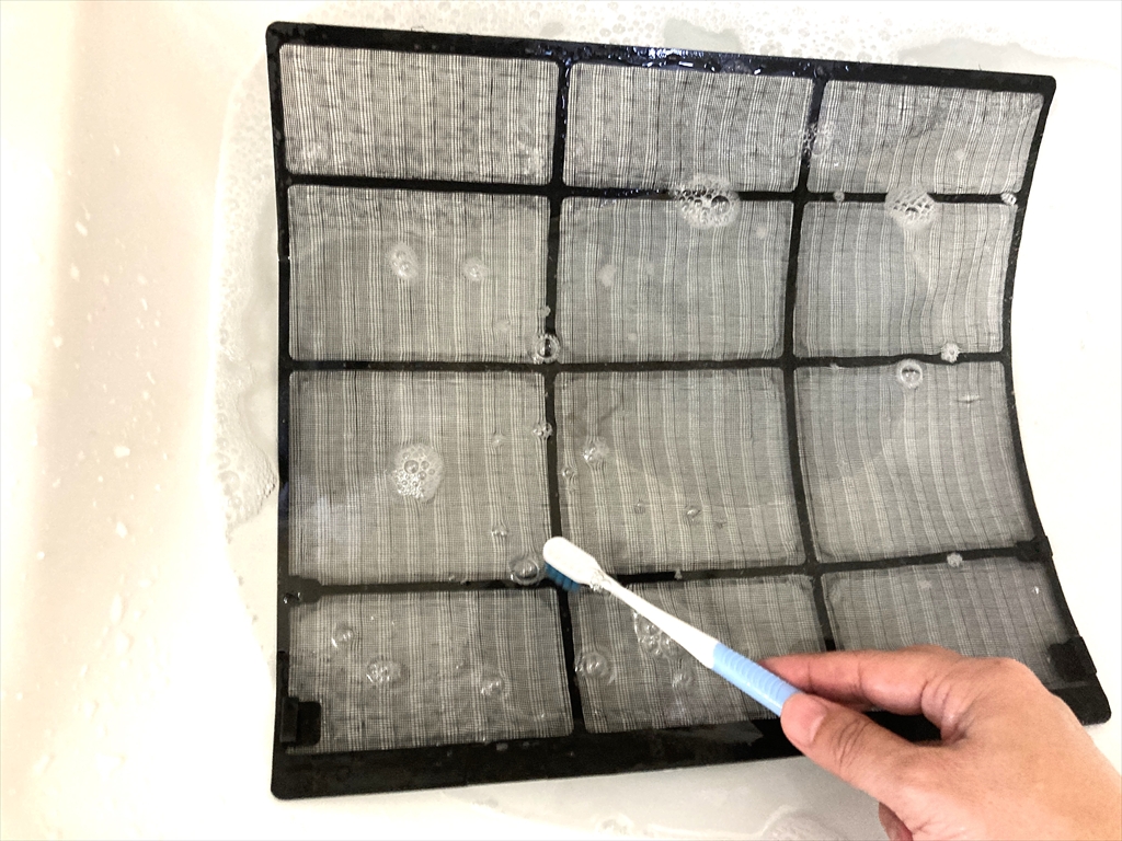 エアコンフィルターを柔らかいブラシでこすり洗いしている様子