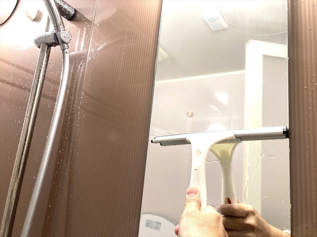 スクレイパーを使って鏡の水滴を取り除いている様子