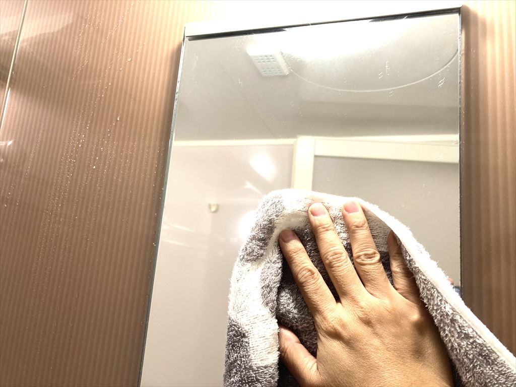タオルで鏡の水気を拭きとっている様子