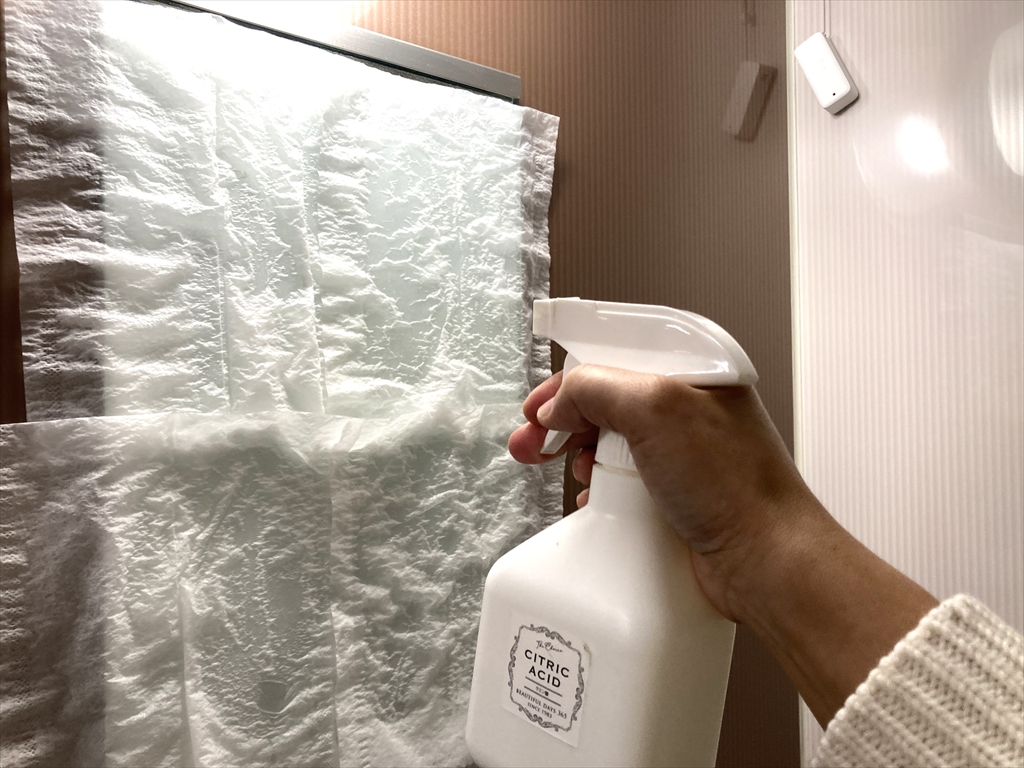 鏡にキッチンペーパーを貼り付けて、上からクエン酸スプレーを塗布している様子