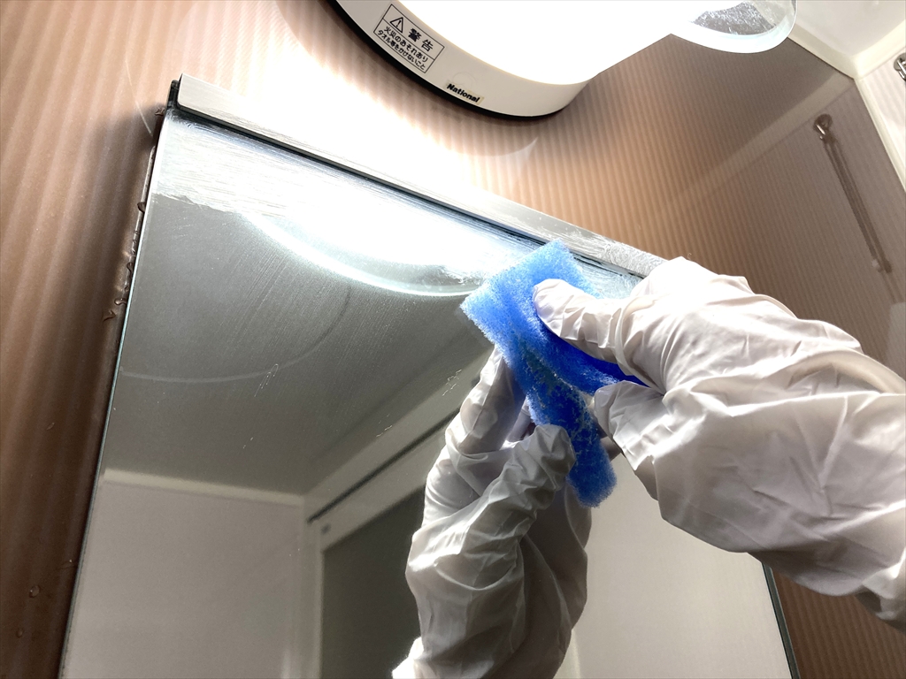 水垢専用洗剤を使って鏡をこすり洗いしている様子