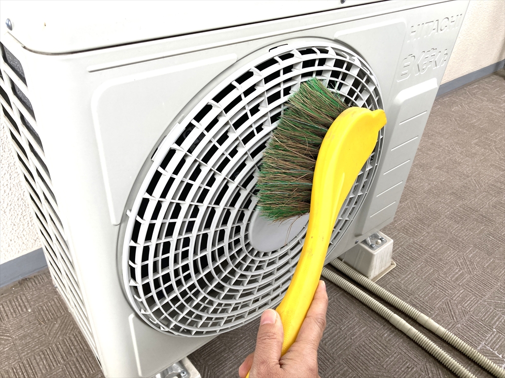 エアコン室外機の前面を、ブラシを使って汚れを落としている様子