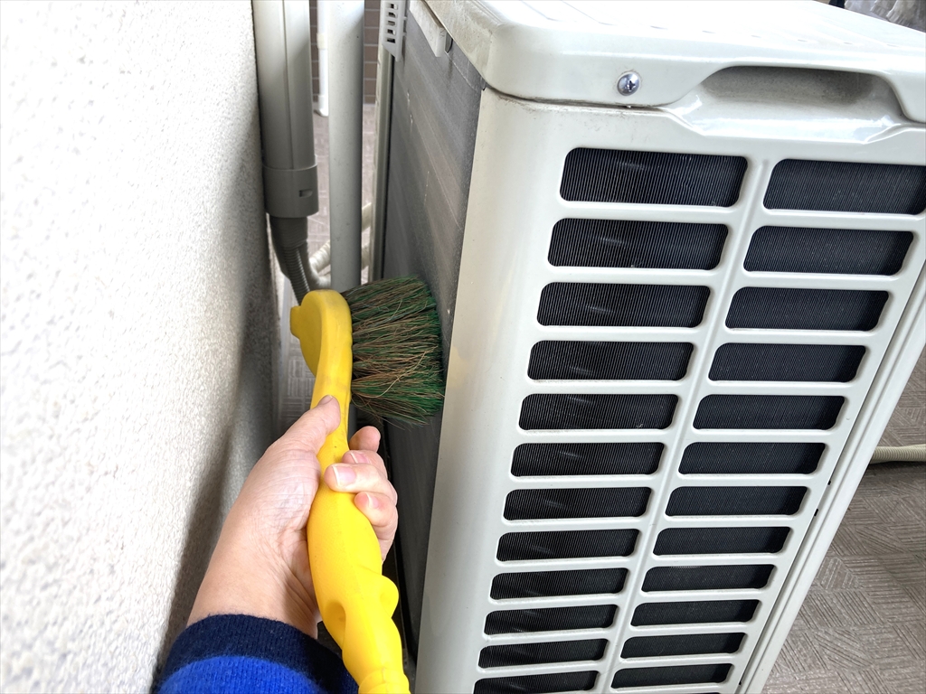 エアコン室外機の背面にあるアルミフィンをブラシでやさしく掃除している様子