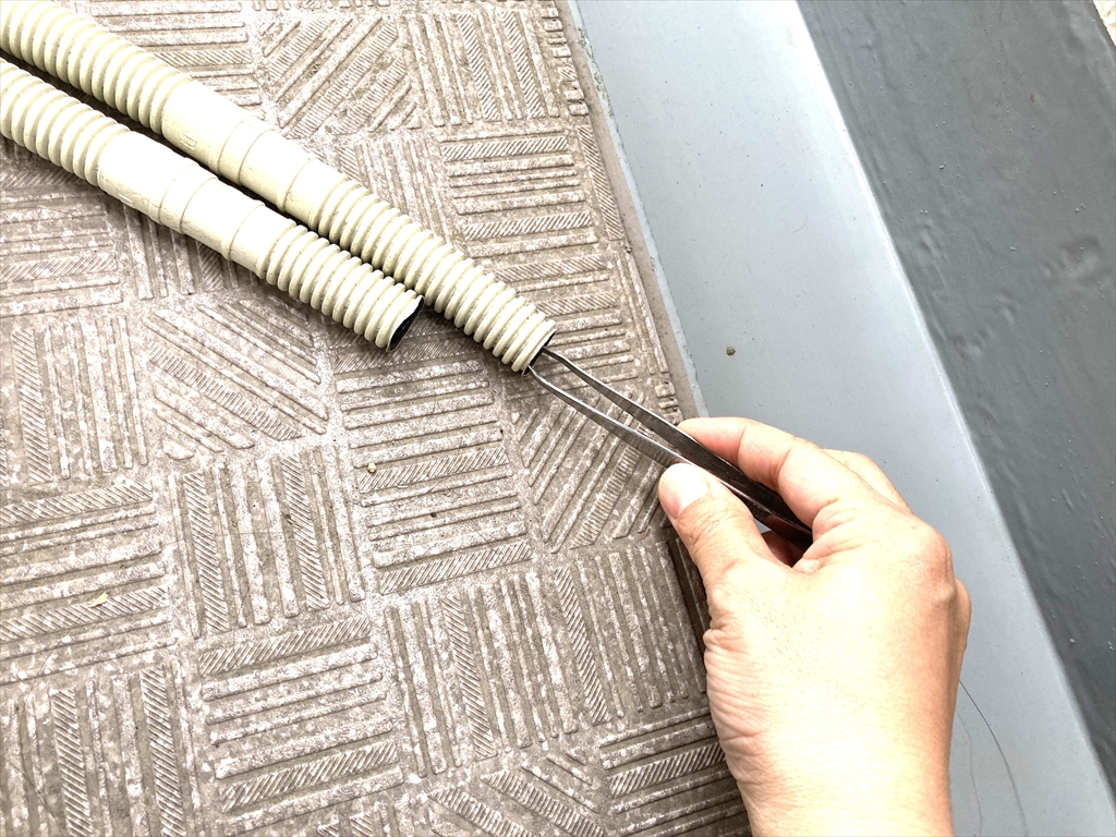 エアコン室外機についているドレンホースのなかに残ったゴミをピンセットでつまんでいる様子