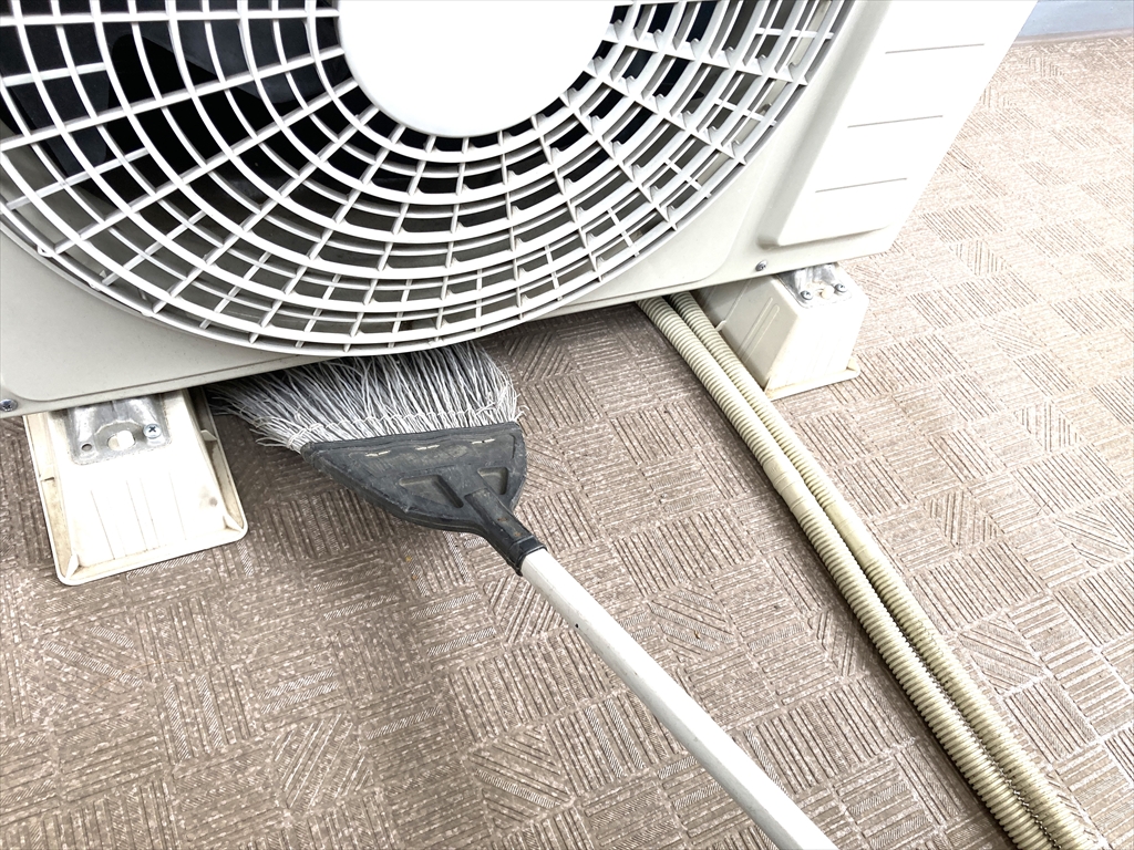 エアコン室外機の下をホウキで掃いている様子