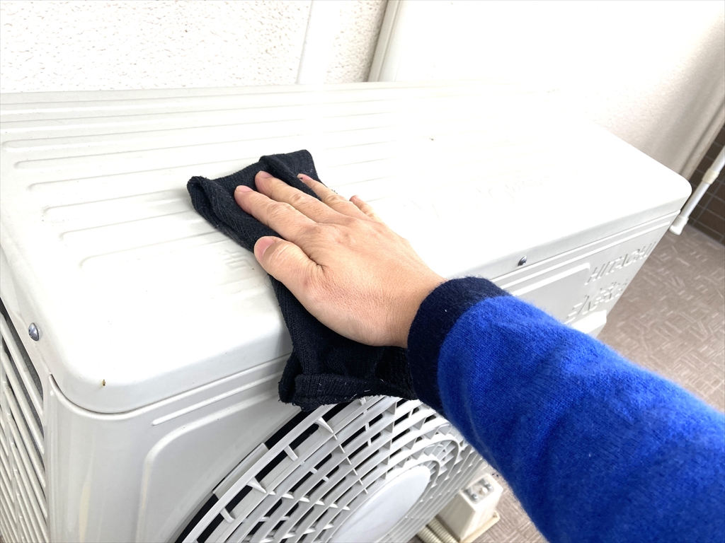 エアコン室外機の上部を布で拭いている様子