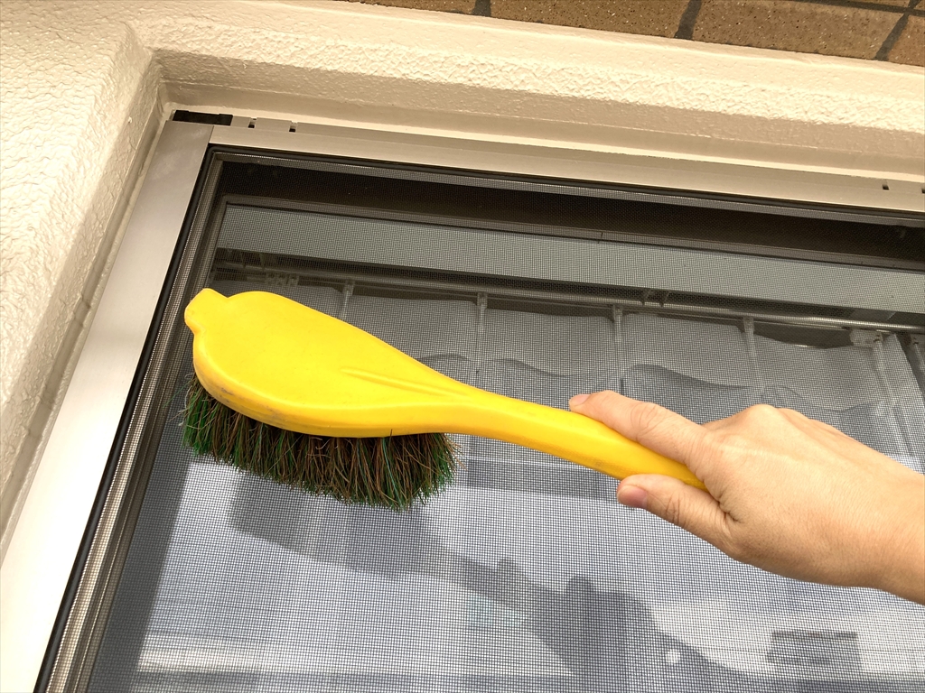 洗車ブラシで網戸をやさしくこすって、汚れを落としている様子
