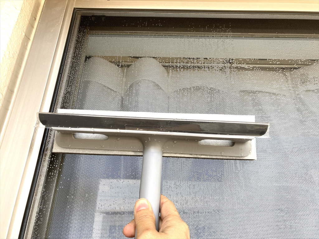 濡らしたクリーナーで網戸をやさしくこすっている様子