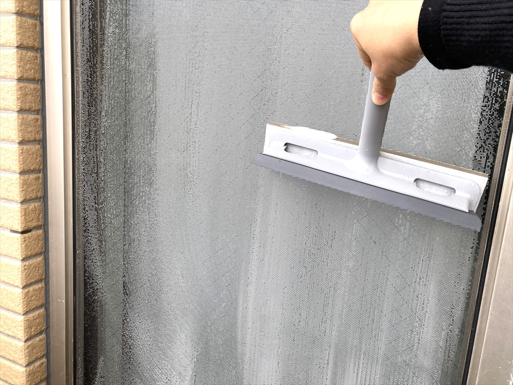 網戸の下側を、クリーナーを下向きにしてこすっている様子
