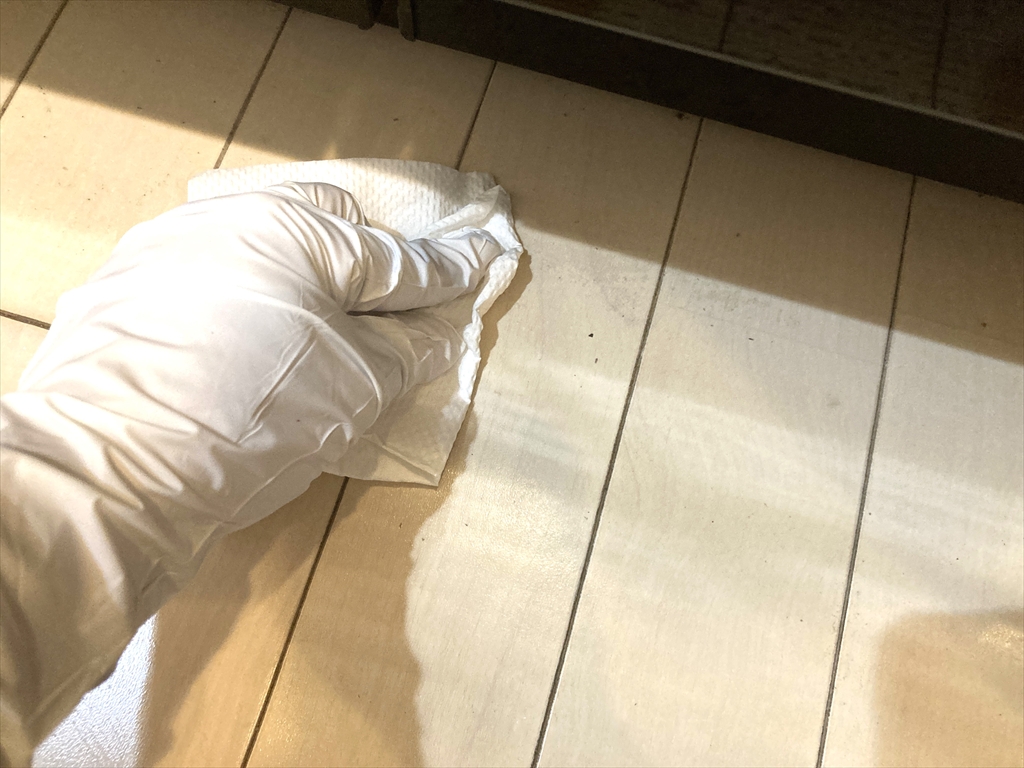 キッチンの床にスプレーしたアルコールを乾いた紙で拭きとっている様子