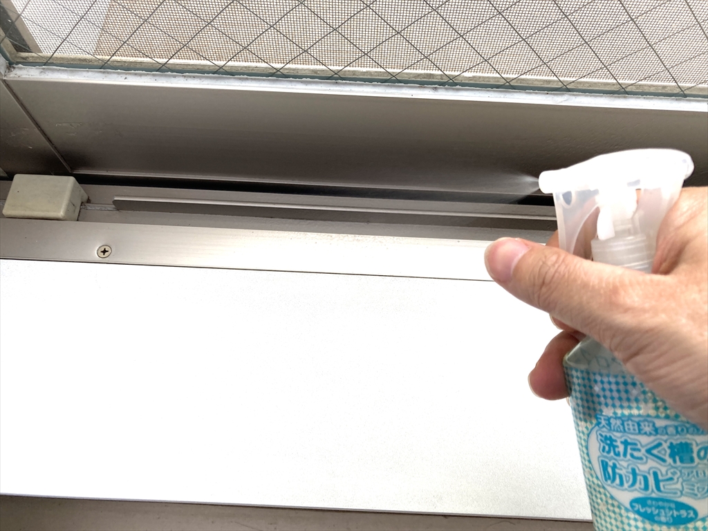 窓の冊子に洗濯槽用防カビスプレーを噴射している様子