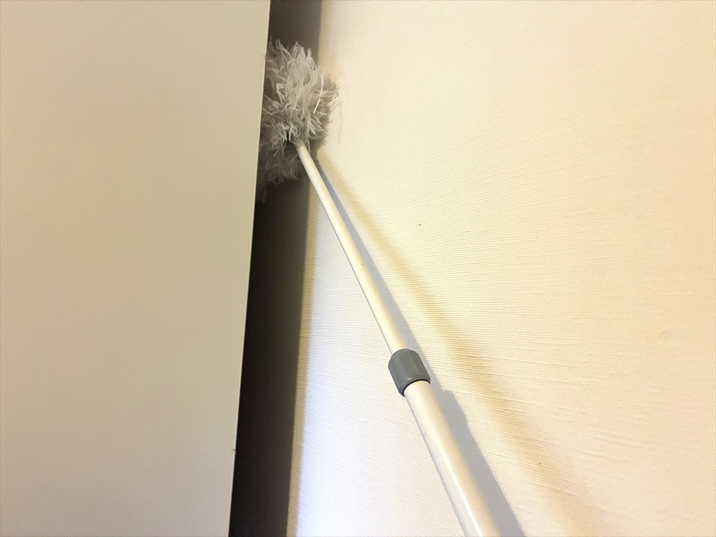 食器棚の側面にあるスキマに、柄の長いモップを入れて掃除している様子